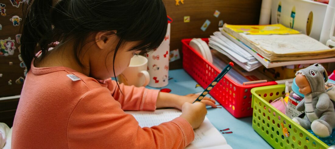 girl in pink long sleeve shirt writing on white paper