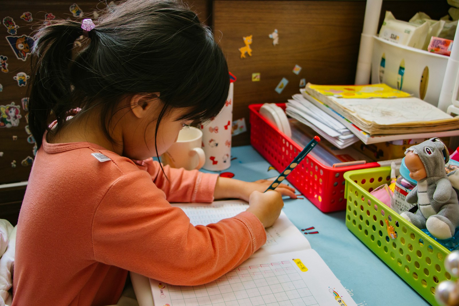 girl in pink long sleeve shirt writing on white paper